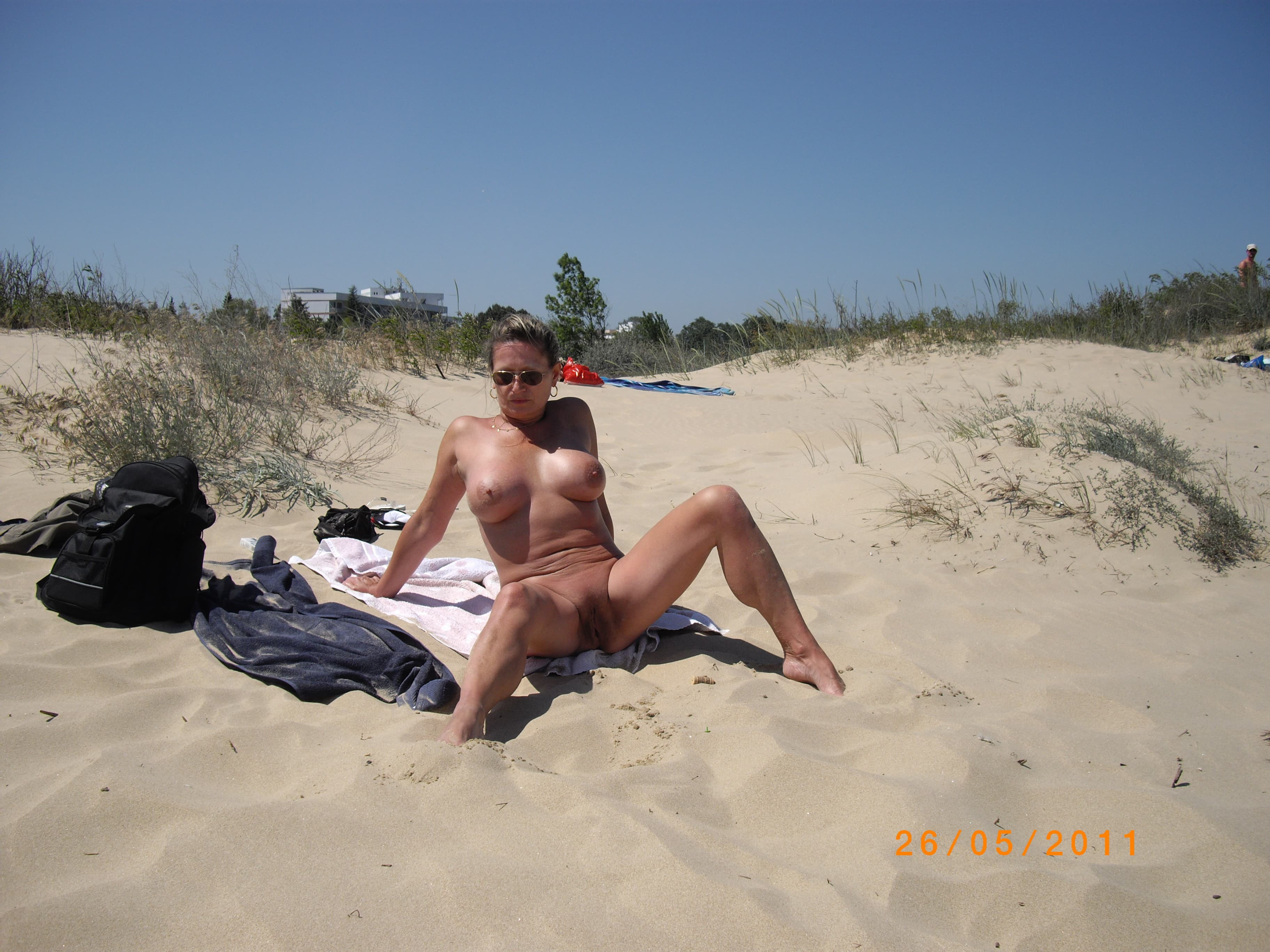 Зрелая голая нудистка загорает на пляже - фото