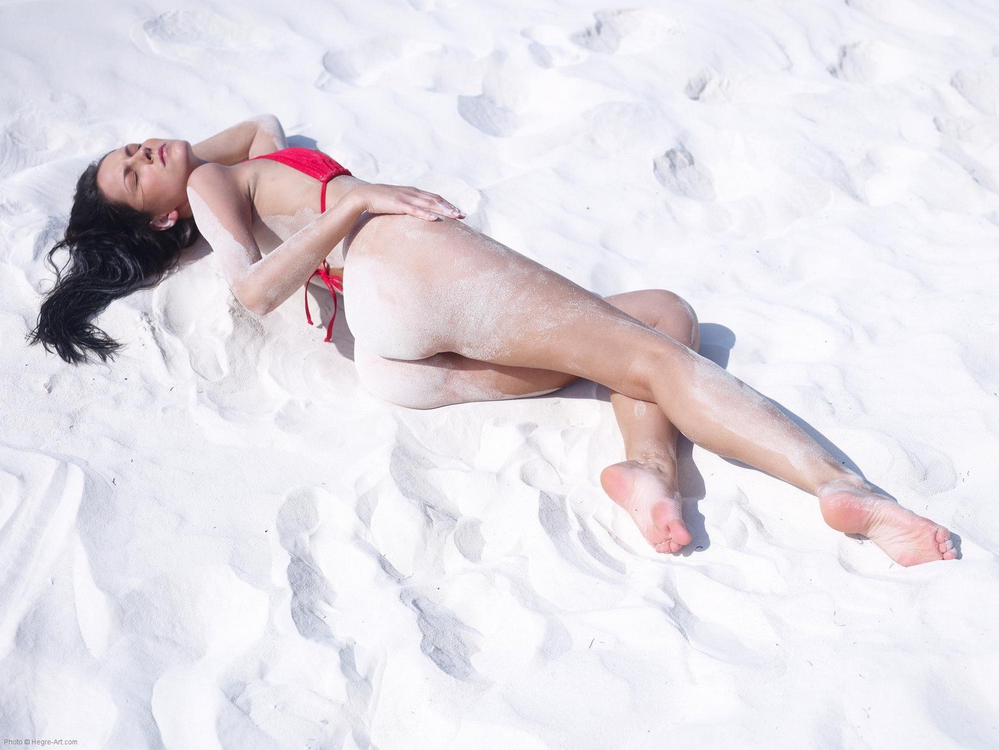 Брюнетка в красном купальнике с голой жопой в песке - фото